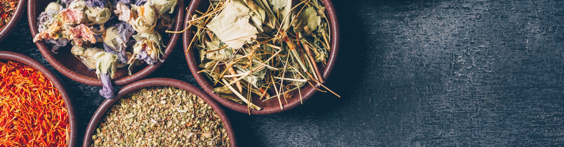 Some tea herbs in a bowls on dark textured background, top view. space for text